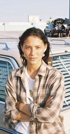 a woman standing in front of a car with her arms crossed