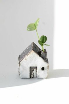 a small white house with a plant growing out of it's roof, against a white background