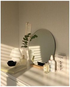 a mirror sitting on top of a white dresser next to a lamp and vase with a plant