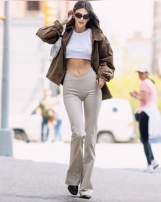 a woman walking down the street with her jacket over her shoulder and sunglasses on top