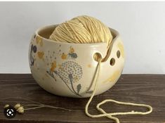 a ball of yarn in a bowl on a wooden table next to a knitting needle