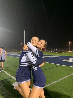 two young women hugging each other on a soccer field at night with lights in the background