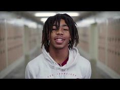 a young man with dreadlocks standing in a long hallway wearing a white hoodie