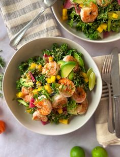 two bowls filled with shrimp and vegetables next to silver utensils on a table