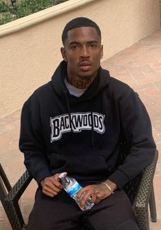 a man sitting in a chair holding a water bottle and wearing a black hoodie