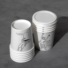 two cups with cartoon drawings on them sitting next to each other in front of a gray background