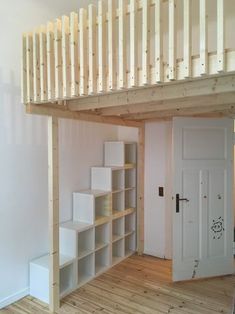 a loft bed with shelves underneath it in a room that has white walls and wooden floors