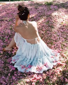 a woman sitting on the ground in a field of flowers with her back to the camera