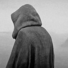 a person in a hooded jacket looking out at the ocean on a foggy day