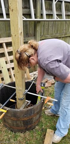 a woman bending over to pick up something out of a barrel in the yard,