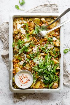 a white dish filled with vegetables and garnished with sauce on the side next to a fork