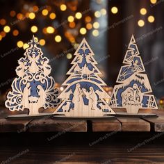 three wooden christmas trees on a table with lights in the background