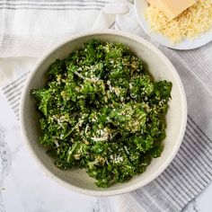 a white bowl filled with green vegetables next to a plate of cheese