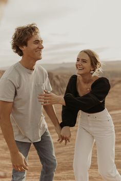 a man and woman walking in the desert holding each other's hands while smiling