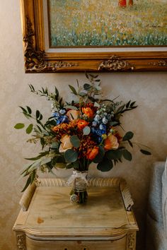 a vase filled with flowers sitting on top of a table next to a painting and chair