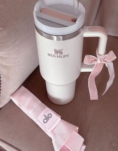 a white travel mug sitting on top of a brown couch next to a pink ribbon