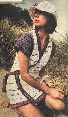 a woman sitting on top of a sandy beach next to grass and sand dunes wearing a white crocheted dress