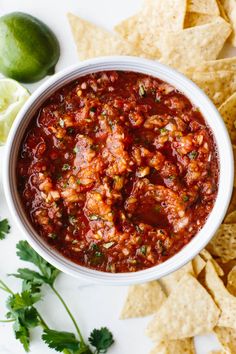 a white bowl filled with salsa surrounded by tortilla chips and cilantro