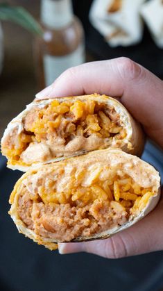 a hand holding two burritos with cheese and other toppings on top of them