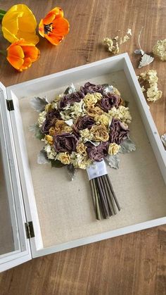 a bouquet of flowers sitting in a white box on a wooden table next to some dried flowers