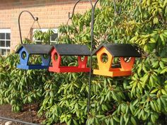 three colorful bird houses are hanging from a wire in front of some bushes and trees