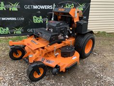 an orange lawn mower sitting on top of gravel next to a sign that says getmowers