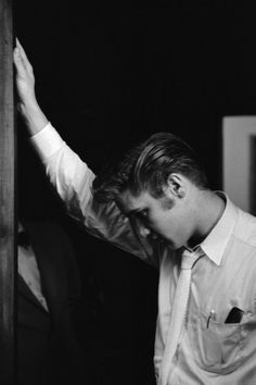 black and white photograph of a man holding his hand up in the air while standing next to a door