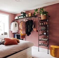 a bedroom with pink walls and clothes hanging on the rack in front of a bed