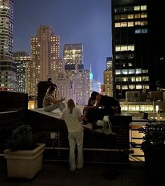 three people standing on top of a roof in front of the city skyline at night