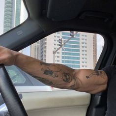 a man with tattoos on his arm sitting in the driver's seat of a car