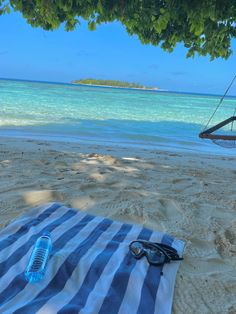 a blue and white striped towel on the beach under a tree with sunglasses laying on it