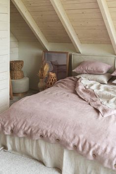 a bed with pink linens and pillows in a lofted room next to a window