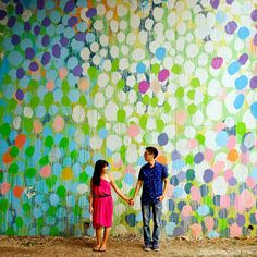 a man and woman holding hands in front of a wall with colorful circles painted on it