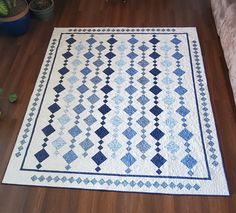 a blue and white quilt sitting on top of a wooden floor next to a potted plant