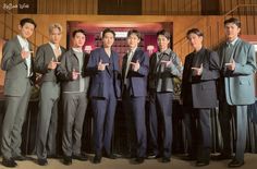 a group of men standing next to each other in front of a wooden wall holding their thumbs up