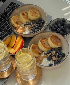 three plates with fruit and pastries on them next to two glasses of water near a laptop