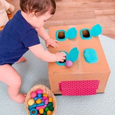 a small child playing with some toys on the floor in front of a cardboard box