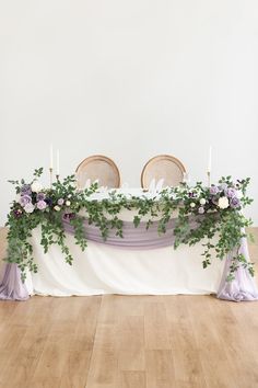 an arrangement of flowers and greenery on a table with two chairs at the end