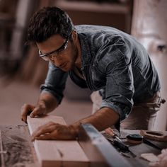 a man in glasses working on wood with a planer and other items around him