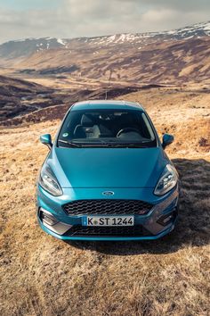 a blue car parked on top of a dry grass field