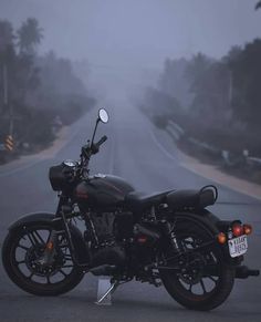 a black motorcycle parked on the side of a road in the middle of foggy day