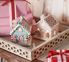 two gingerbread houses are on a tray with presents in the background and one has a red bow