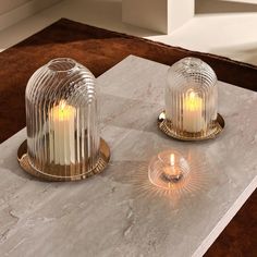 two glass candles are sitting on a marble table with a brown rug in the background