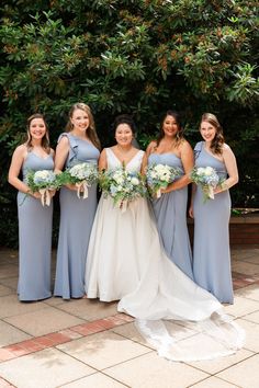 a group of women standing next to each other in front of some bushes and trees