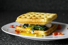 a waffle sandwich on a white plate topped with cheese and spinach toppings