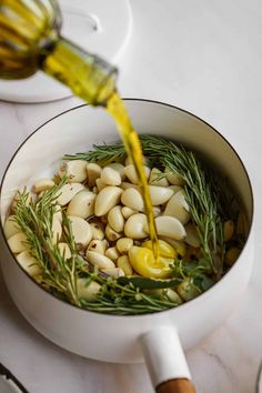 someone is pouring olive oil on some food in a pot with rosemary sprigs