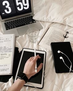 a person using an electronic device on top of a bed with books and headphones