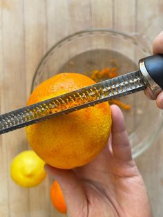 someone is peeling an orange with a large knife on top of it and some lemons in the background