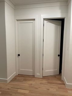 an empty room with two white doors and hard wood floors