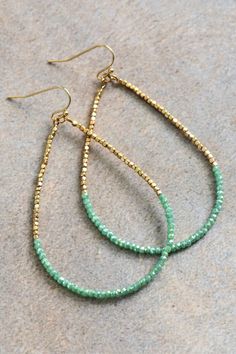 two pairs of gold and green beaded hoop earrings on top of a gray surface